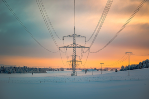 Versorgungssicherheit der Schweiz - Sonnenuntergang im Hintergrund, davor ein Strommast mit Leitungen, die auf den Betrachter zu laufen